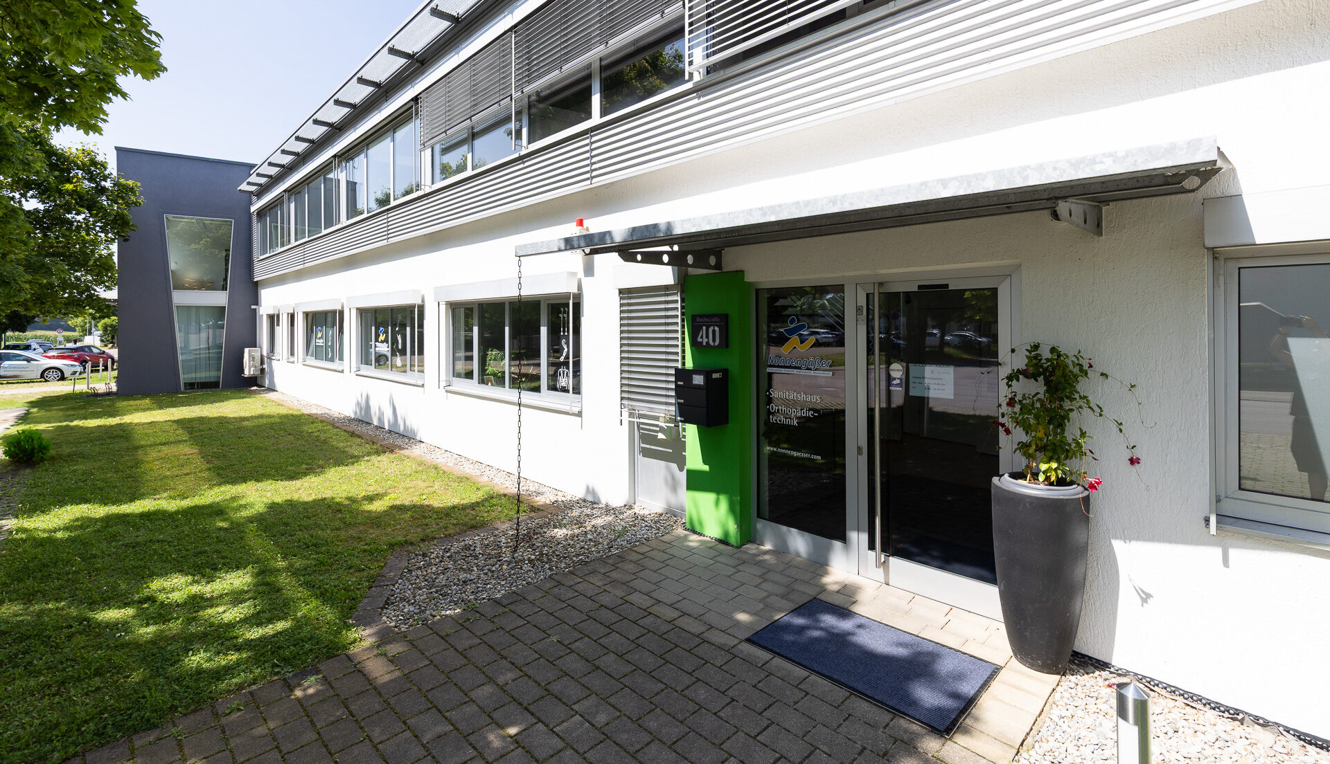 Ansicht des Eingangsbereiches von Nonnengäßer Orthopädietechnik in Donzdorf – Glastür mit Briefkasten links daneben und einem Blumenkübel